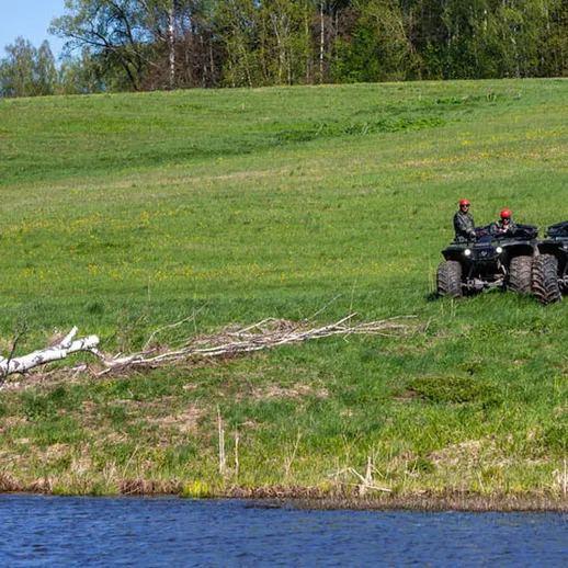 Работающие квадроциклы на берегу реки весной на фоне зелёного луга и леса