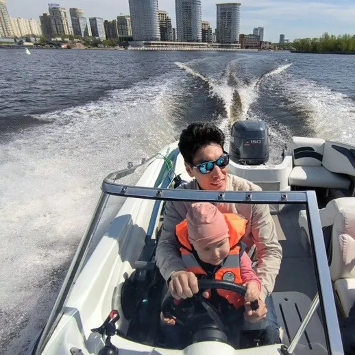 Папа управляет лодкой с маленьким ребенком на реке в городе в ясный день весной