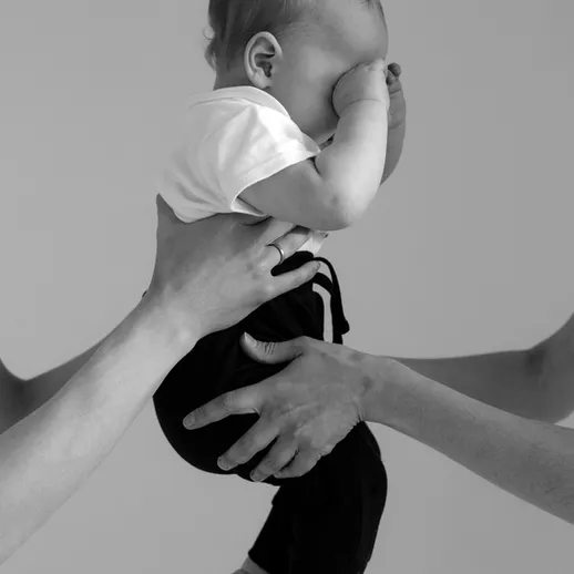 Младенец с зажмуренными глазами в руках у родителей на нейтральном фоне