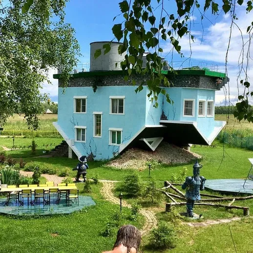 Странный дом с уникальным дизайном в зеленом ландшафте под ярким небом