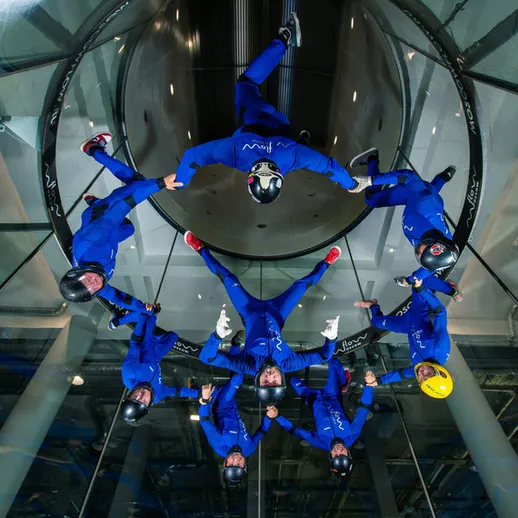 Группа людей выполняет параллельные акробатические элементы в аэродинамической трубе в современном развлекательном центре