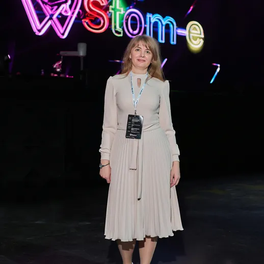 Женщина в светлом платье стоит на мероприятии с яркой вывеской в Москве