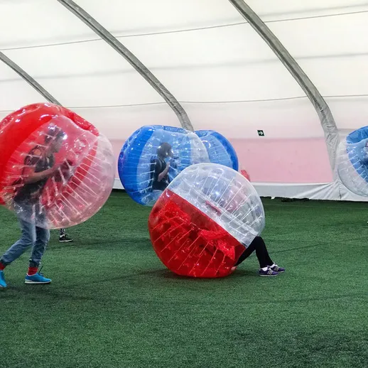 Участники играют в бамперный футбол в закрытом зале на зеленом газоне под крытой конструкцией