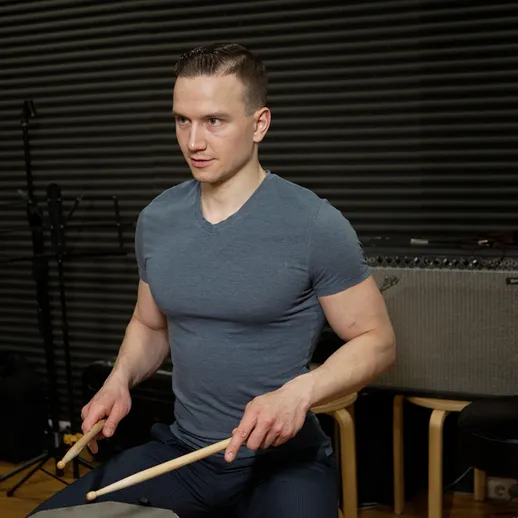 Молодой мужчина играет на барабанах в репетиционной студии среди музыкального оборудования