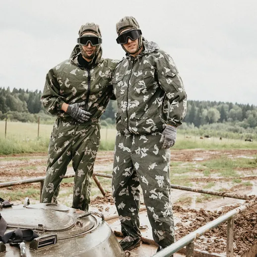 Два военнослужащих в камуфляжной форме на танке во время учений на фоне леса и грязных дорожек