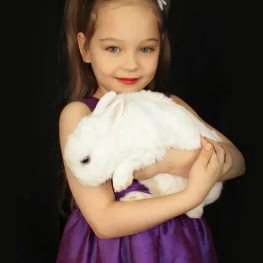 Девочка в фиолетовом платье держит белого кролика на черном фоне на фотосессии