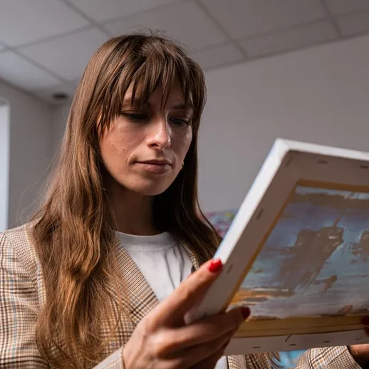 Женщина внимательно рассматривает картину в художественной студии во время дневного света