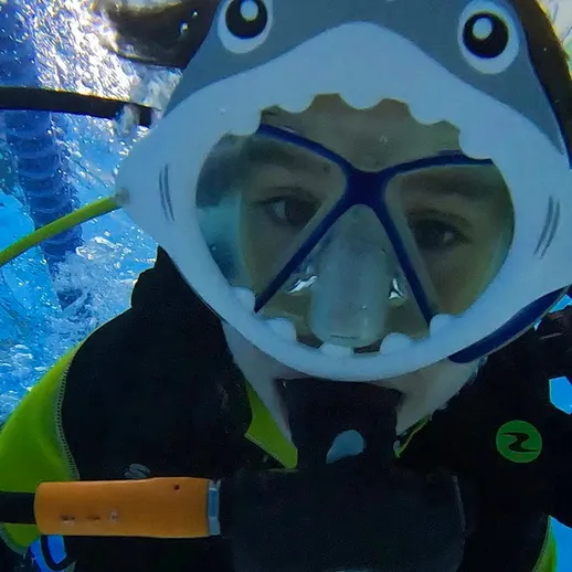Ребенок в маске для сноркелинга с дизайном акулы под водой в аквариуме