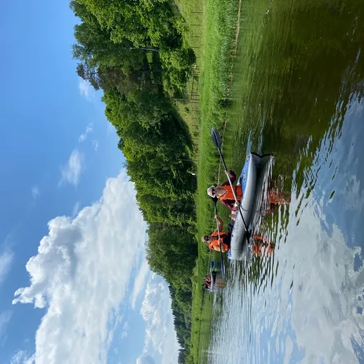 Групповая экскурсия на каяках по спокойной реке в окружении зелёных лесов и ясного неба в летний день