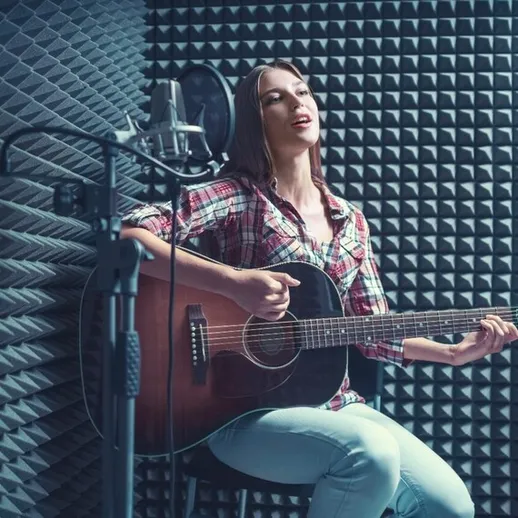 Молодая женщина поет и играет на гитаре в звукозаписывающей студии