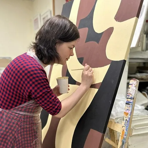 Женщина пишет картину в художественной мастерской, используя кисть и акриловые краски, в спокойной обстановке