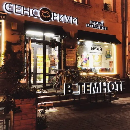 Сенсорный музей «В темноте» на улице в вечернее время, освещенный яркими огнями и притягивающий внимание прохожих