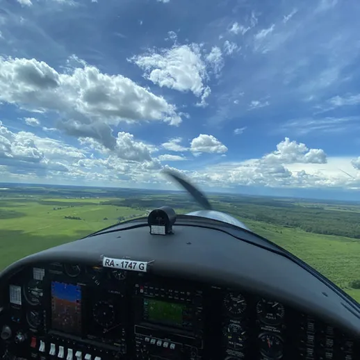 Вид из кабины самолета над зелеными полями и облачным небом в солнечный день