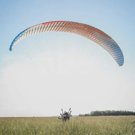 Парапланерист парит над зелеными полями в солнечный день на фоне ясного неба