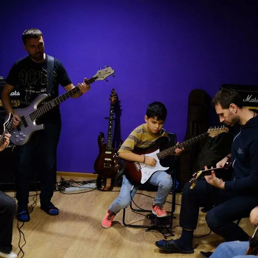 Урок музыки в репетиционной студии с группой музыкантов и юным гитаристом