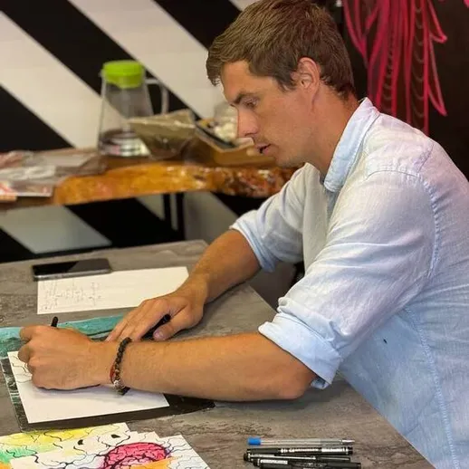 Мужчина рисует на столе в творческой студии с яркими цветами и инструментами в руках