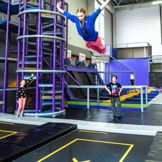 Девочка прыгает с высоты на батуте в развлекательном центре, радостные дети наблюдают за ней