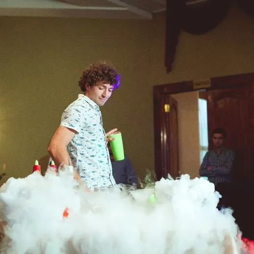 Молодой человек с коктейлем на вечеринке, окруженный туманом, в зале для мероприятий