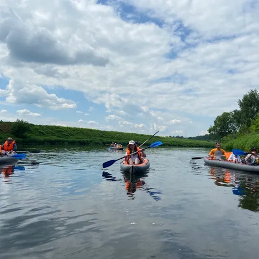Групповая каякинговая прогулка по реке в солнечный день с красивыми облаками и зелеными деревьями