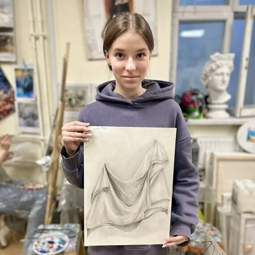 Девочка держит натюрморт с тканью в художественной мастерской во время урока рисования