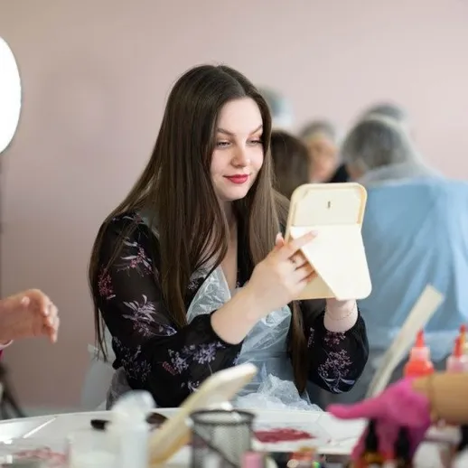 Девушка смотрит в зеркало во время занятия по макияжу