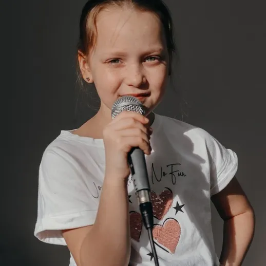 Девочка поет на сцене, держа микрофон, в студии для записи музыки