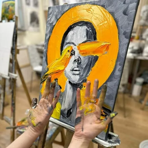 Молодая художница создает яркую картину с портретом на фоне оранжевого круга в студии