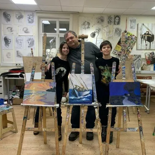 Два ребенка и взрослый человек в художественной студии с картинами на мольбертах в спокойной обстановке