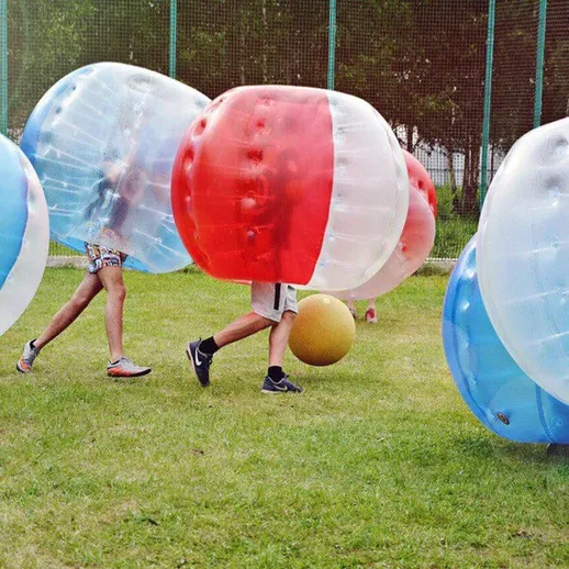 Игроки в шарах для бамперного футбола на зеленом поле во время активного отдыха с мячом