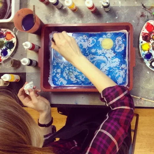 Женщина создает уникальную марморированную бумагу с использованием красок в мастерской