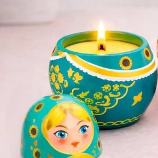 Свеча в форме матрешки и маленькая матрешка на столе с ярким светом