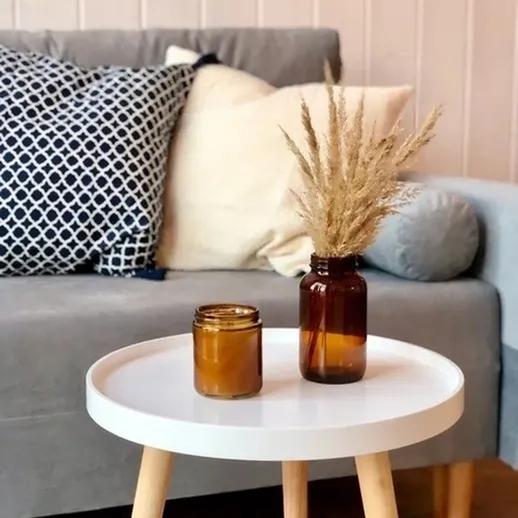 Стильная композиция с вазой и свечой на столике в уютной комнате с серым диваном