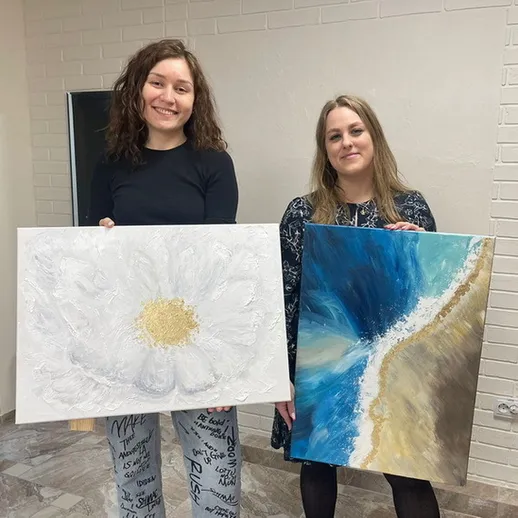 Две художницы показывают свои картины в помещении, одна с цветком, другая с морем