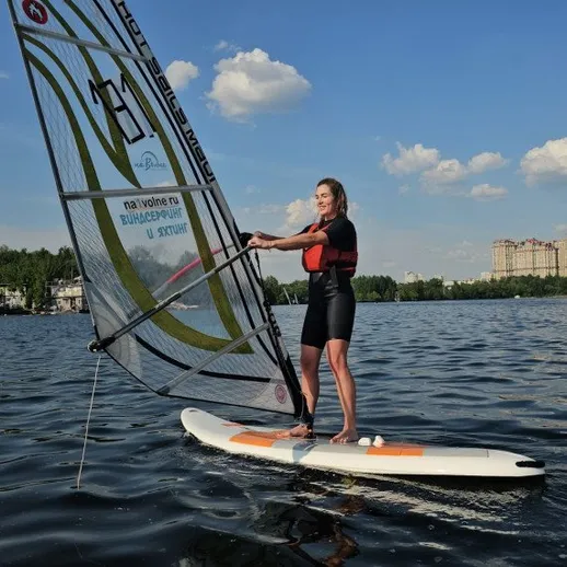 Серфер стоит на доске с парусом на воде в городе в ясный день