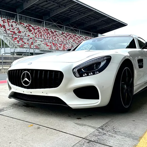 Белый спортивный автомобиль на гоночной трассе с трибунами в ясный день