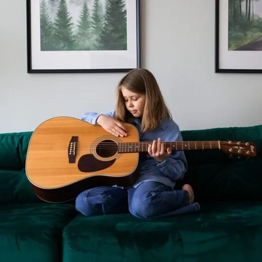Девочка играет на гитаре на диване в уютной комнате с зелёным интерьером