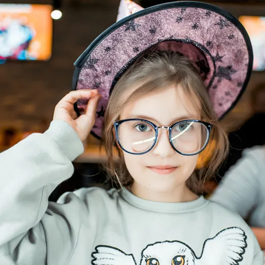 Девочка в очках и шляпе с ведьмовским мотивом в кафе во время праздника