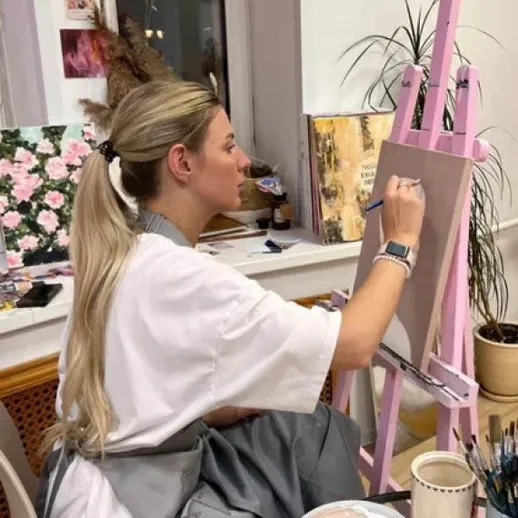 Женщина рисует на холсте в уютной студии с яркими растениями и картинками на стенах