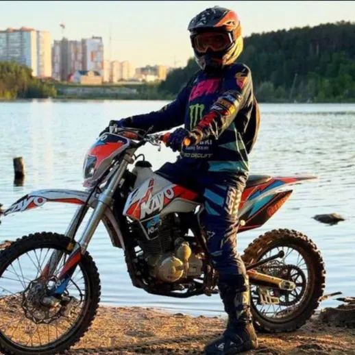 Мальчик на мотоцикле стоит у воды на закате в городе