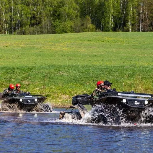 Два амфибийных транспорта пересекают реку среди зелёной природы в ясный день