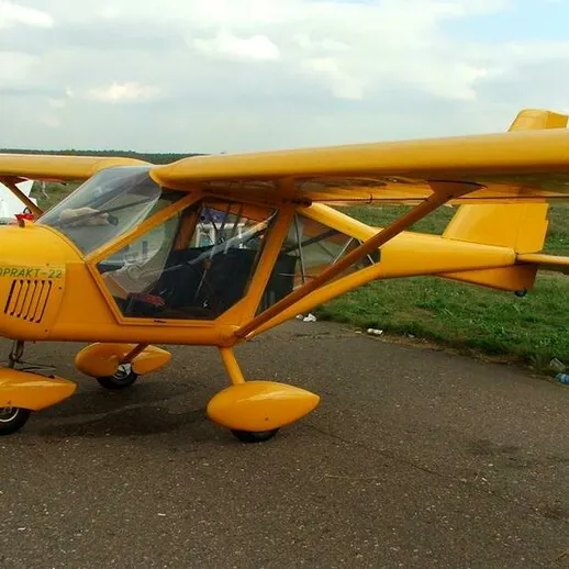 Желтый легкий самолет стоит на взлетно-посадочной полосе небольшого аэродрома в солнечный день