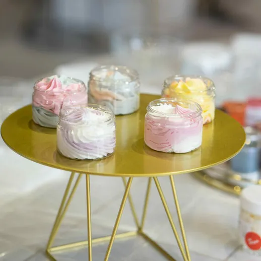 На круглой подставке расположены кремовые десерты различных цветов на фоне современного интерьера