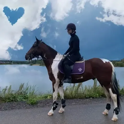 Наездница верхом на коне у озера под облаками в форме сердца в солнечный день