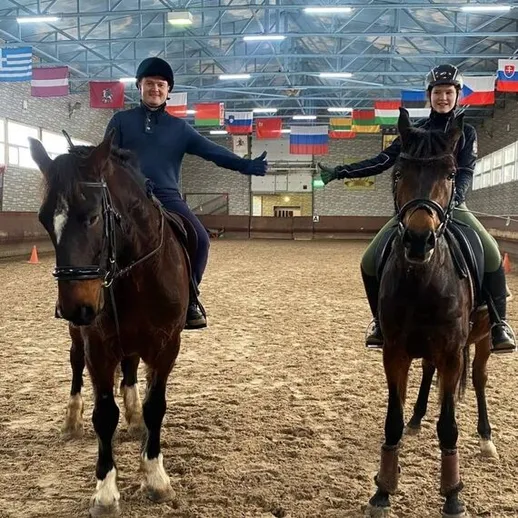 Урок верховой езды в крытом манеже с двумя всадниками и лошадьми в спортивной школе