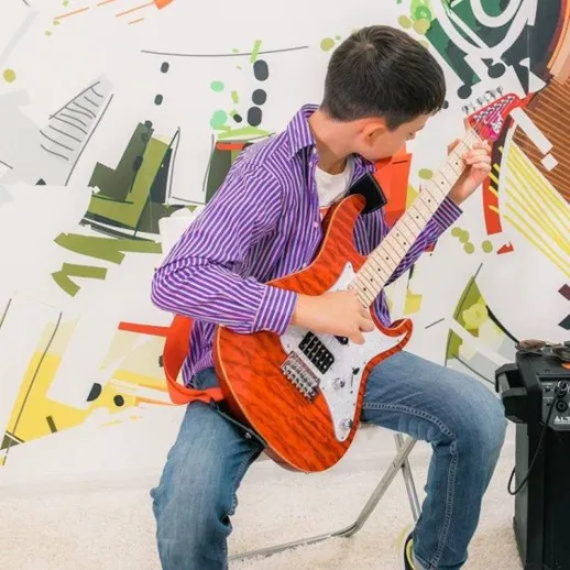 Мальчик играет на гитаре в комнате с яркими стенами и стулом