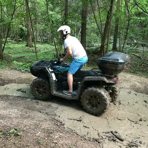 Мужчина на квадроцикле преодолевает грязь в лесу в летний день