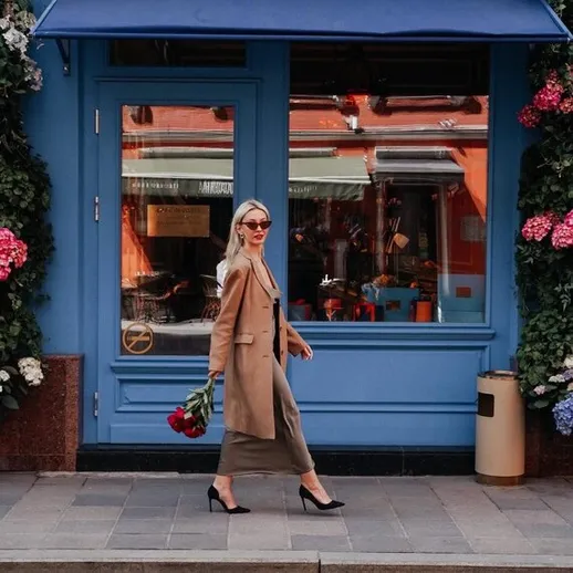 Женщина с цветами идет по улице возле кафе в день с ясным небом