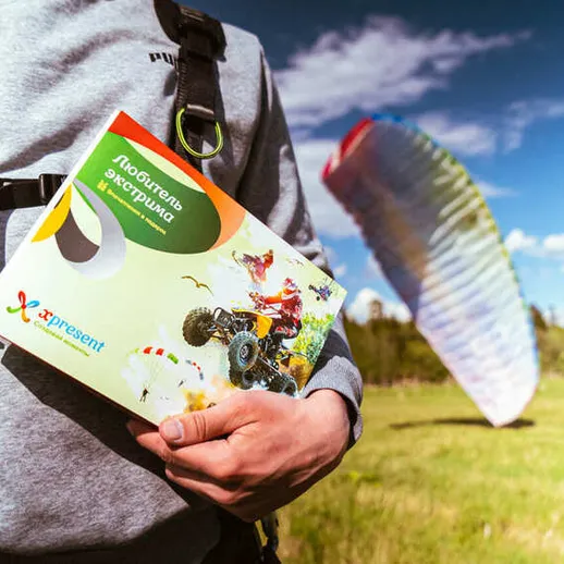 Человек с книжкой о парапланеризме на фоне открытого поля с летящим парапланом в ясный день