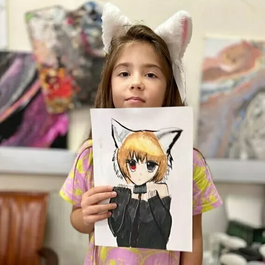 Девочка с кошачьими ушками, держащая рисунок персонажа в костюме, в художественной студии
