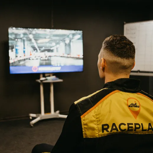 Мужчина в экипировке наблюдает за трансляцией гонок на большом экране в помещении в Racing Place